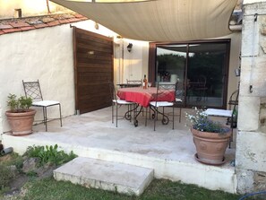 An outdoor patio with a table and chairs, a potted plant, and a sliding glass door leading to an interior space. - Small farmhouse with  AC in the Alpilles, 15 mn  baux de Provence, 3mn  Mouries (Saint-Martin-De-Crau)