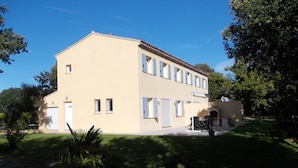 Un edificio a due piani con tetto piatto e facciata beige. È presente una zona esterna coperta con tavoli e sedie.