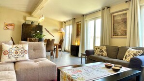 Ein geräumiges Wohnzimmer mit einer Couch, einem Esstisch und einem Couchtisch. Ein Kamin, eine Lampe und ein Gemälde an der Wand sind ebenfalls vorhanden.