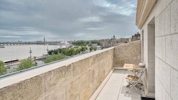 Ein Balkon mit Blick auf einen Fluss, ein Boot und historische Gebäude.