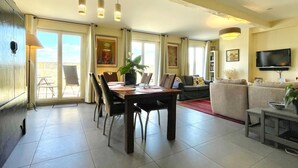 Ein geräumiger Wohnbereich mit Esstisch, Stühlen, einer Couch, einem Fernseher und einem Balkon mit Blick.