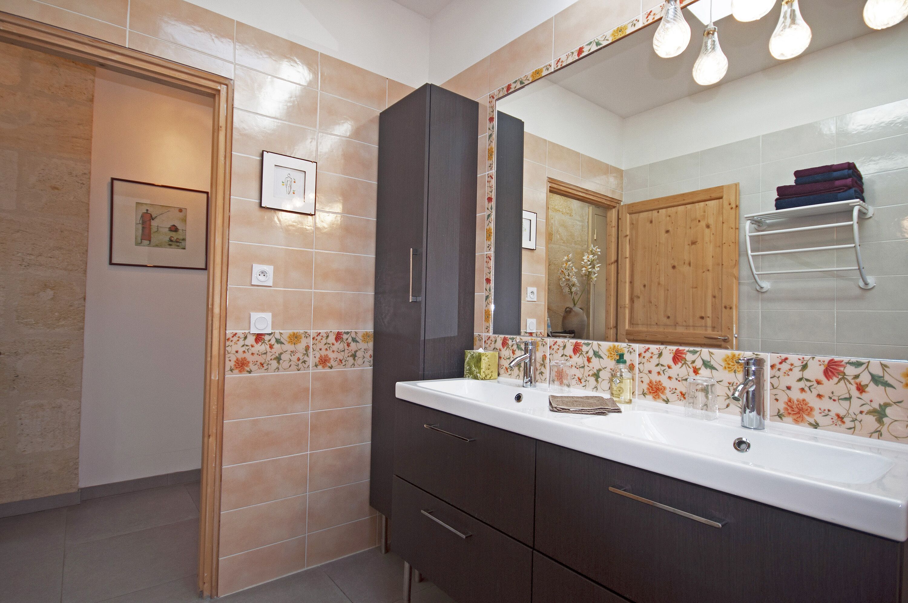 A bathroom with a double sink, dark cabinets, and a mirror with light fixtures.