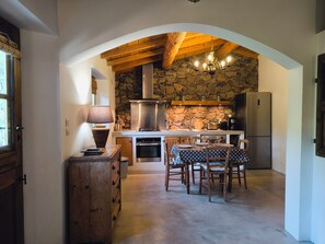 Een gezellige keuken met een stenen muur, houten balken in het plafond en een eethoek met een tafel en stoelen.