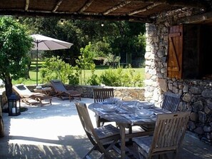 Een terras buiten met een stenen muur, een gedekte tafel en loungestoelen.