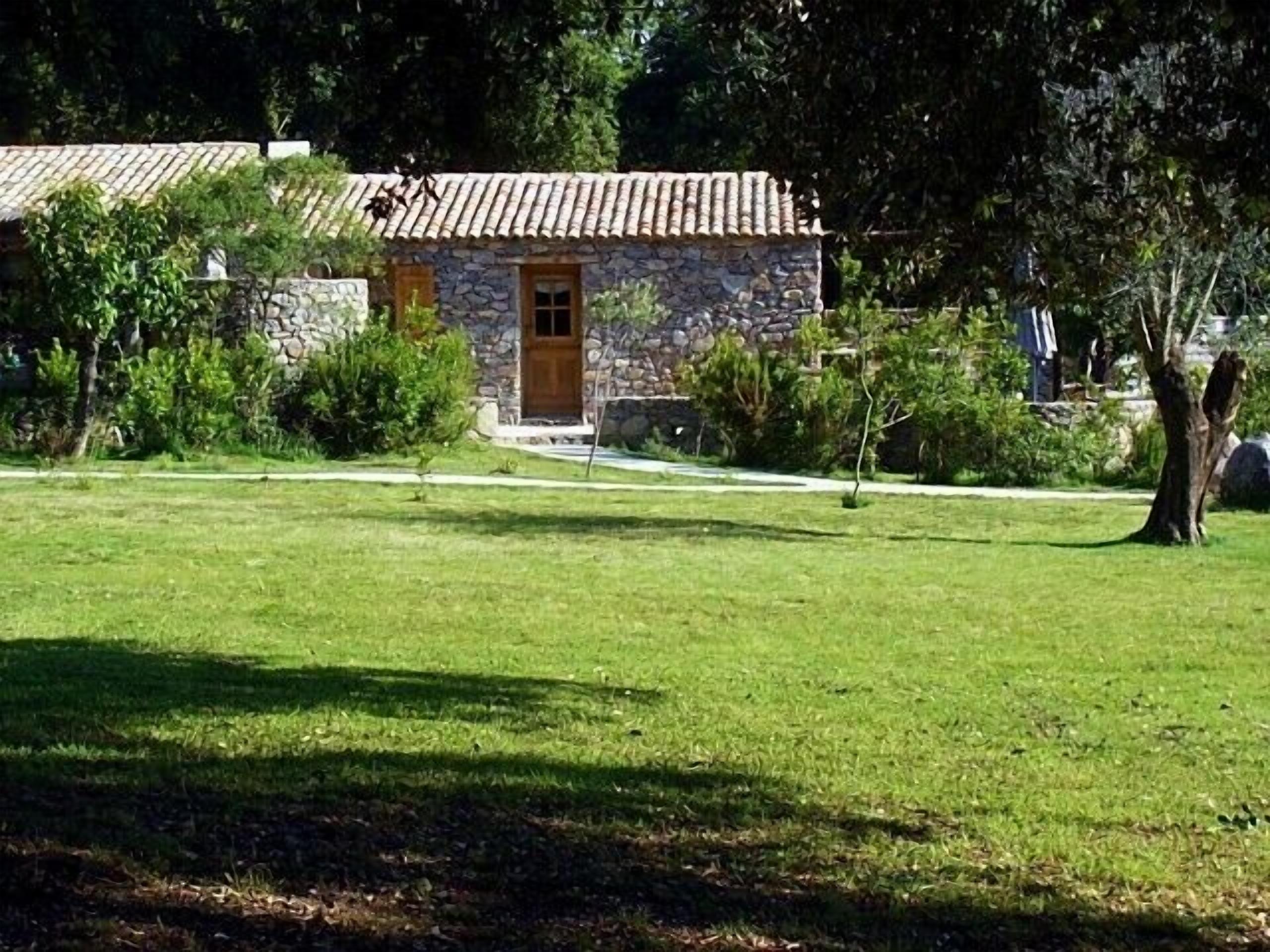A stone building with a tiled roof, surrounded by a well-maintained lawn and various shrubs.