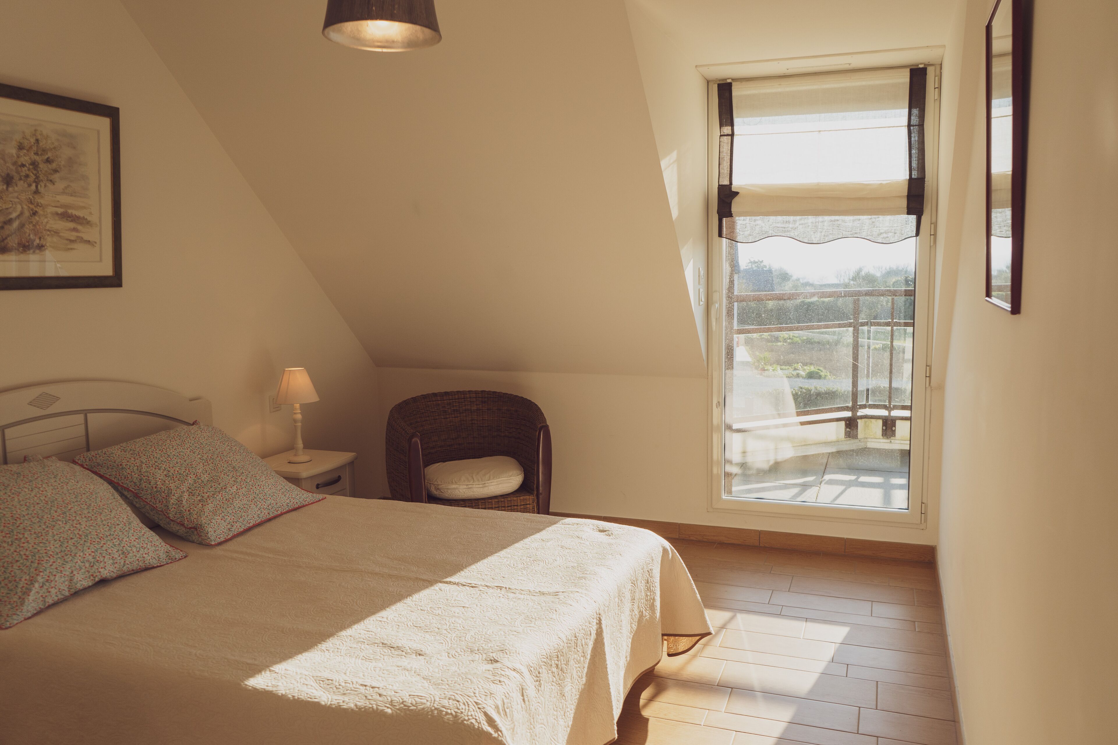A bedroom with a bed, a chair, a nightstand, a lamp, and a window with a view.