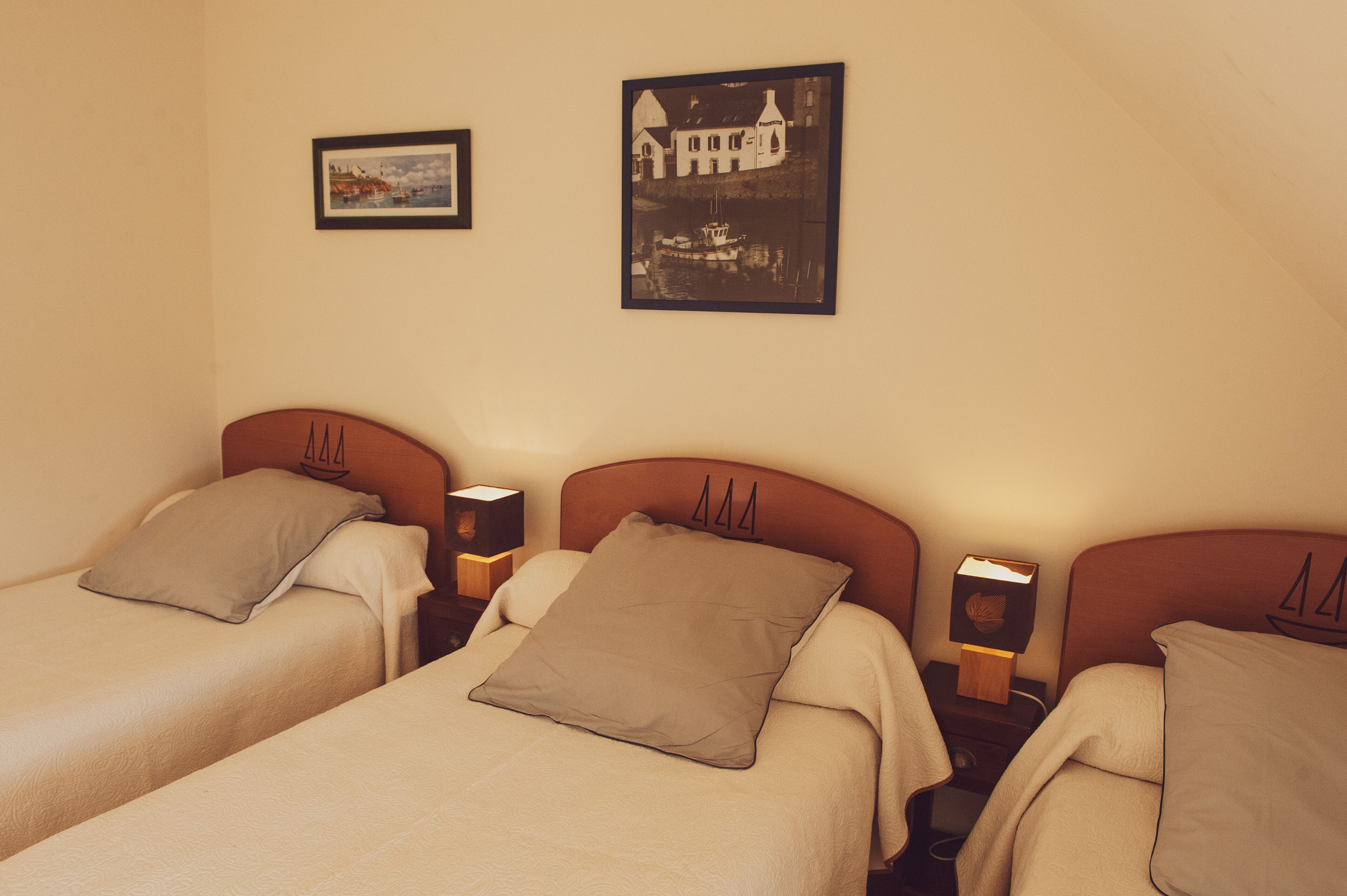 Habitación de hotel con dos camas individuales, cada una con cabecero de madera y un almohadón. Hay dos mesitas de noche con lámparas y un cuadro enmarcado en la pared sobre las camas.