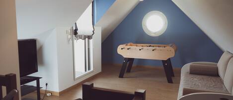 A room with a foosball table, a sofa, a television, and a window with a view of the sky.
