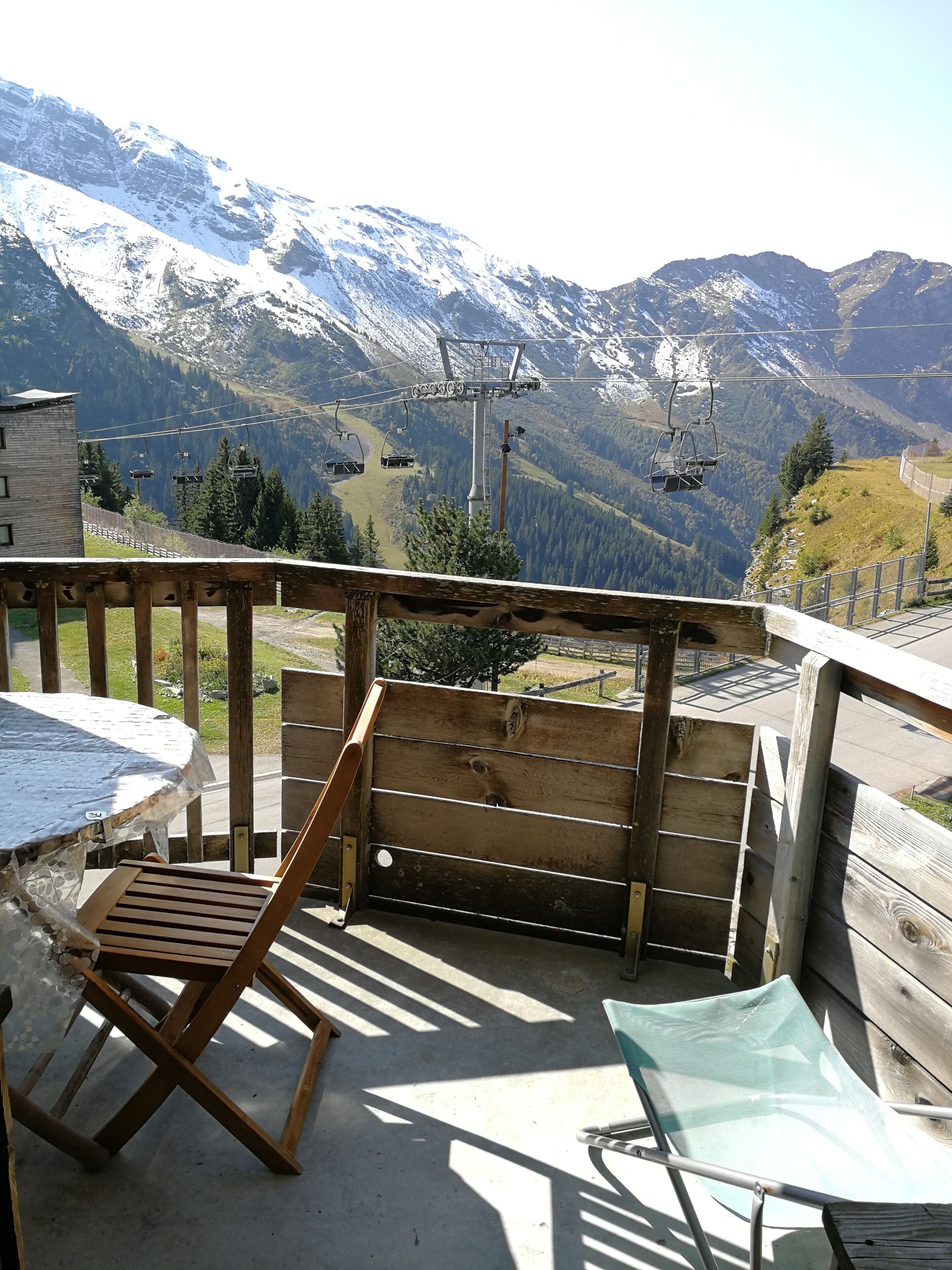 A wooden deck with a table and chairs overlooking a mountainous landscape with ski lifts.