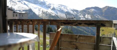 Un balcon en bois avec une table et une chaise, d’où l’on peut admirer des montagnes enneigées.