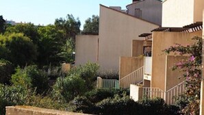 A residential building with a flat roof, a visible staircase, and a garden area with various plants. - Charming T1 completely renovated, with large terrace, in the heart of Giens. (Hyères)