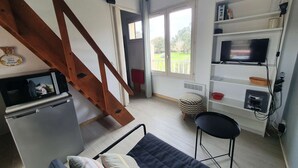 A compact living space with a kitchenette, a sofa, a TV, and a staircase. - Charming T1 completely renovated, with large terrace, in the heart of Giens. (Hyères)