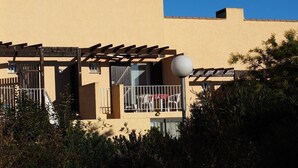 A building with a beige exterior, a balcony with white chairs, and a street lamp in front. - Charming T1 completely renovated, with large terrace, in the heart of Giens. (Hyères)