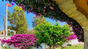A garden with a stone archway, lush green grass, and flowering plants. - CHARMING AIR-CONDITIONED VILLA WITH PRIVATE POOL, GARDEN, NEAR THE SEA AND SHOPS (ELS POBLETS)