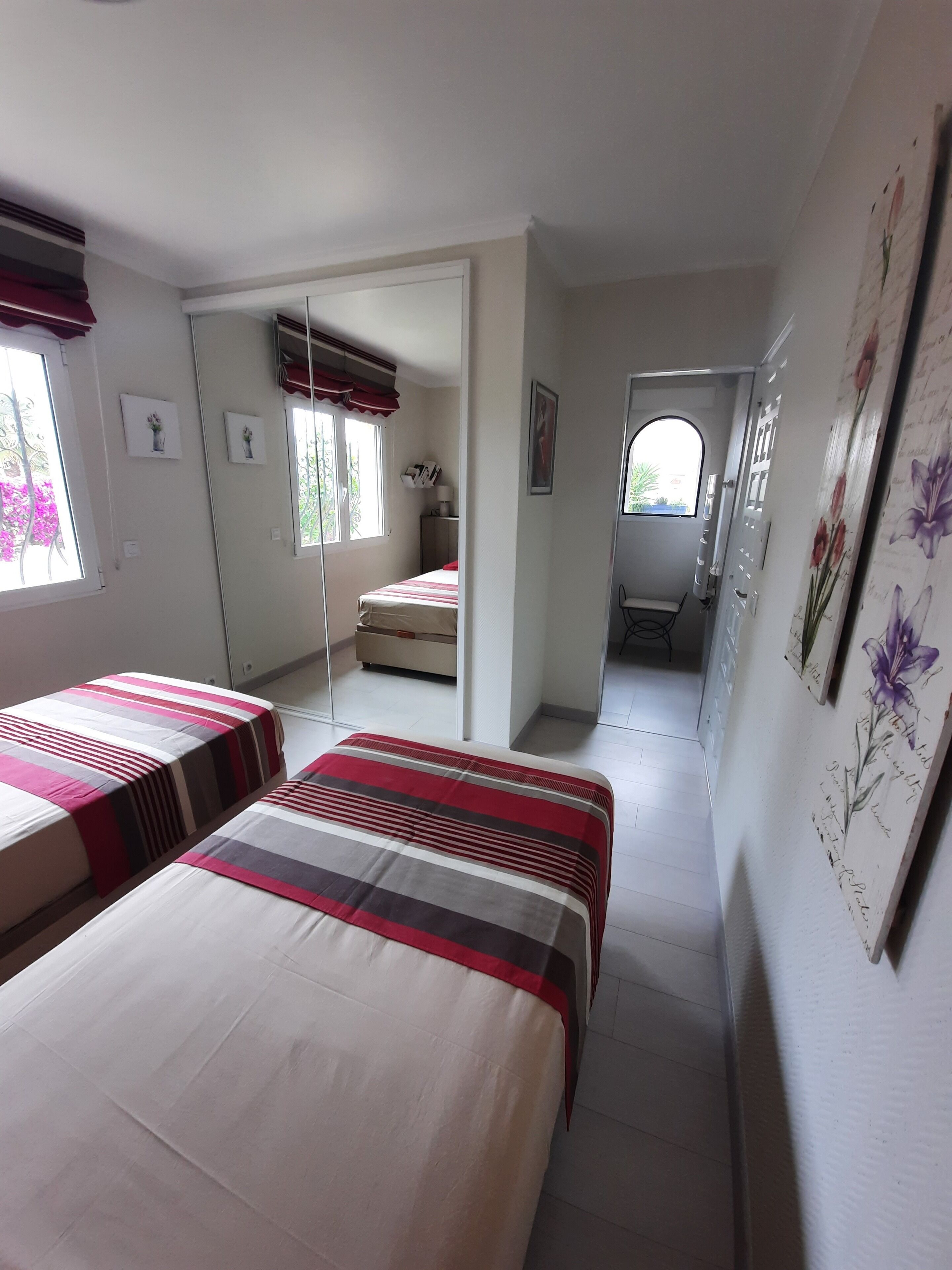 A bedroom with two beds, a mirror, and a door leading to another room.