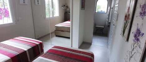 A bedroom with two beds, a mirror, and a door leading to another room.
