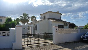 A gated residential area with a white building, a gated entrance, and a parked car. - CHARMING AIR-CONDITIONED VILLA WITH PRIVATE POOL, GARDEN, NEAR THE SEA AND SHOPS (ELS POBLETS)