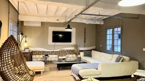 A cozy living room with a hanging chair, a sofa, a TV, and a brick wall.