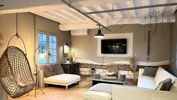 A cozy living room with a hanging chair, a sofa, a coffee table, and a TV mounted on the wall.