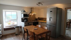 A compact kitchen with a wooden table and chairs, a refrigerator, a microwave, a stove, and a window with a view of the outdoors.