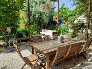 An outdoor patio with a wooden table and chairs, a sofa, and a small garden area with plants and a fountain. - renovated apartment in bourgeois house (Calenzana)