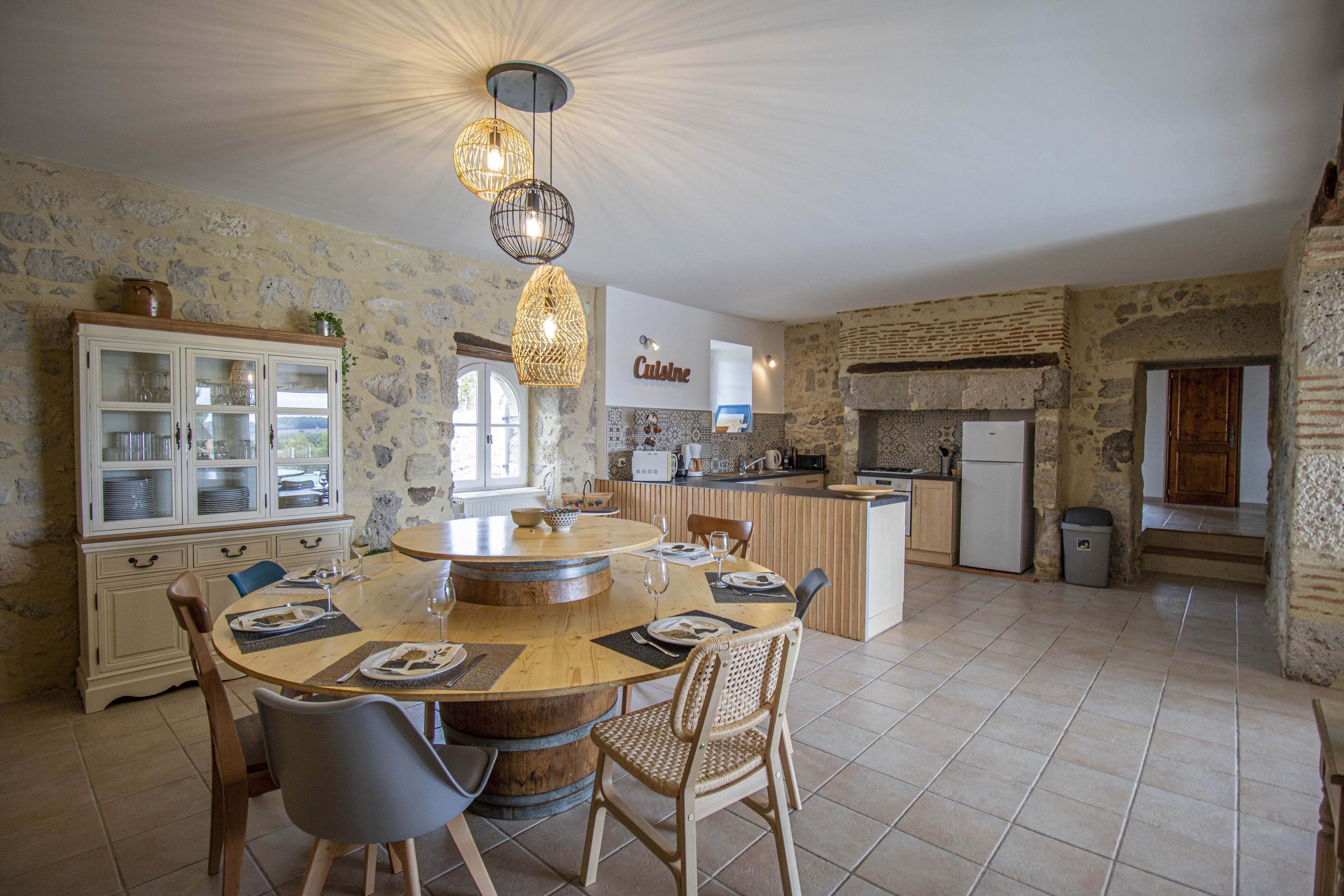 Una cocina amplia con una isla central, paredes de piedra y un comedor con sillas y una mesa.