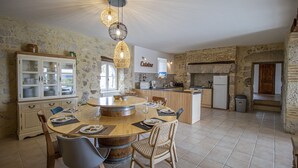 A spacious kitchen with a central island, stone walls, and a dining area with chairs and a table. - Rental in Nerac en Albret, stone built house, detached, renovated. (Nérac)