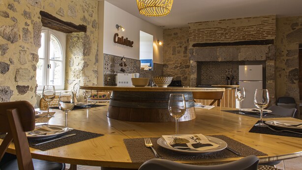 A dining area with a rustic stone wall, a wooden table set for a meal, and a hanging light fixture. - Rental in Nerac en Albret, stone built house, detached, renovated. (Nérac)