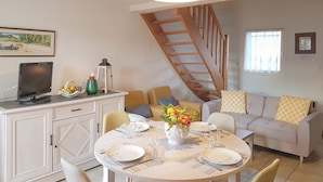 A dining area with a round table set for four, a television on a cabinet, and a staircase in the background. - House with garden by the sea in Pornic. Nearby beach. (Pornic)