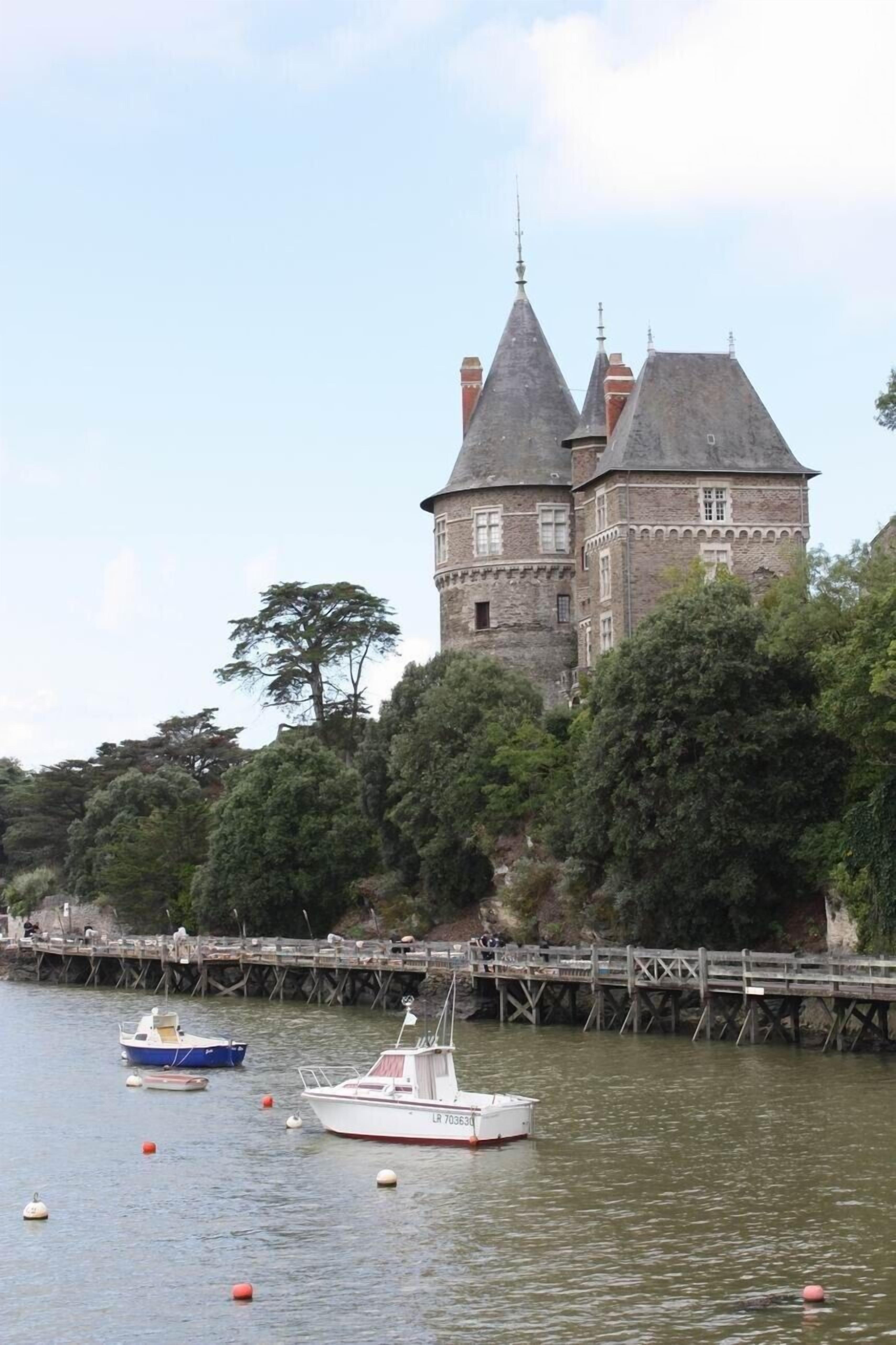 A castle-like building with a tower, surrounded by trees and a wooden dock with boats.