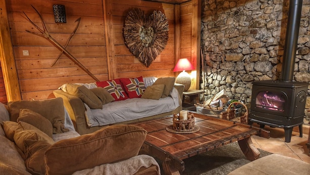 A cozy cabin interior with a stone wall, wooden furniture, a fireplace, and a decorative wall piece. - Chalet Jamoo, an authentic renovated farmhouse in the heart of the Aravis mountains  (Entremont)