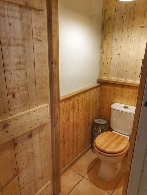 A wooden-paneled bathroom with a toilet and a trash bin.