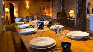 A wooden dining table set with plates, bowls, and wine glasses, with a rustic interior and a fireplace in the background. - Chalet Jamoo, an authentic renovated farmhouse in the heart of the Aravis mountains  (Entremont)