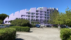 A modern building with a unique architectural design, featuring balconies and a parking lot in front. - Apartment with swimming pool - garage - air conditioning. - beach 200m away - WIFI (La Grande-Motte)