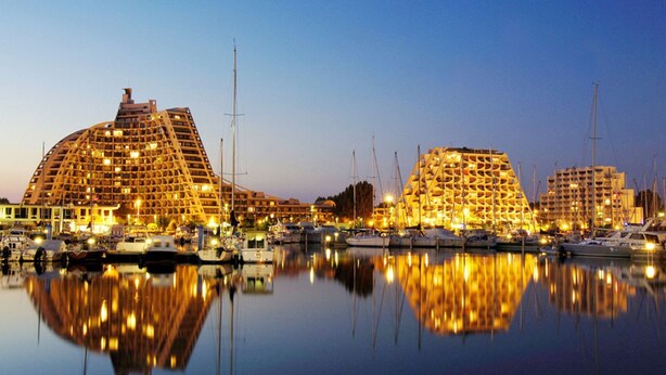 A marina with large, uniquely designed buildings reflecting on calm water. - Apartment with swimming pool - garage - air conditioning. - beach 200m away - WIFI (La Grande-Motte)