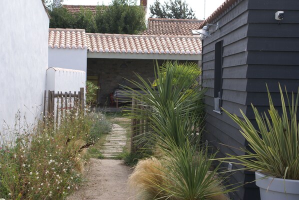 A narrow pathway leading to a house with a tiled roof and a dark siding exterior.