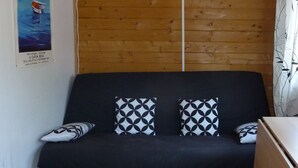 Ein Holzblockbau-Innenraum mit einer schwarzen Couch, gemusterten Kissen und einer Wandmontage-Klimaanlage.
