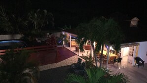 A nighttime view of a resort with outdoor seating areas, palm trees, and a pool.