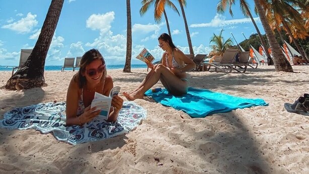 A beach with palm trees, sun, and people relaxing.