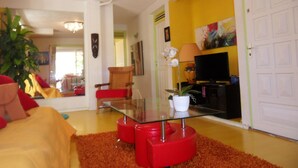 A living room with a glass coffee table, red ottomans, a potted orchid, and a television.