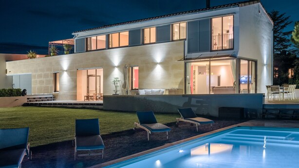 Una casa moderna de dues plantes amb piscina, mobiliari exterior i interior ben il·luminat.