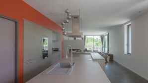 Una cuina moderna amb una illa central, electrodomèstics integrats i grans finestres que deixen entrar llum natural.