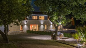 Una casa moderna amb un camí de grava, una zona de barbacoa i una entrada ben il·luminada.