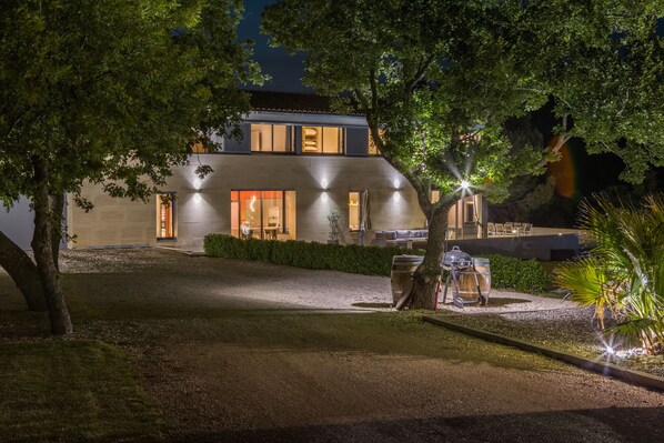 Une maison moderne avec une allée en gravier, un espace barbecue et une entrée bien éclairée.