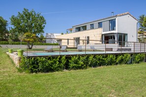 Una casa moderna de dos pisos con piscina, mobiliario exterior y un jardín bien cuidado.