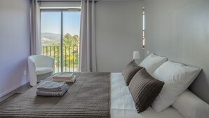Habitació d'hotel amb llit, cadira i balcó que dona als turons.