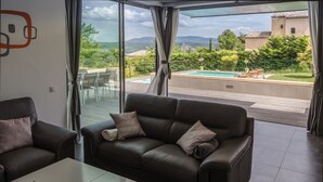 Un saló modern amb un sofà de cuir i una taula de centre, grans portes corredisses de vidre que donen a un balcó amb piscina i vistes panoràmiques.