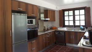 A modern kitchen with wooden cabinets, stainless steel appliances, and a large window providing natural light. - Norman house with pool in the countryside (Bâlines)