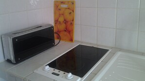 A kitchen with a toaster oven, an induction cooktop, and a yellow cutting board with fruit images.