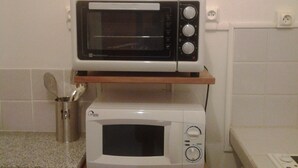 A kitchen with a microwave on a shelf, a spoon in a container, and a power outlet on the wall.